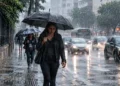 Pessoa caminhando com guarda-chuva durante chuva intensa em área urbana, representando a previsão de chuvas no Sul e Sudeste