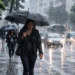 Pessoa caminhando com guarda-chuva durante chuva intensa em área urbana, representando a previsão de chuvas no Sul e Sudeste