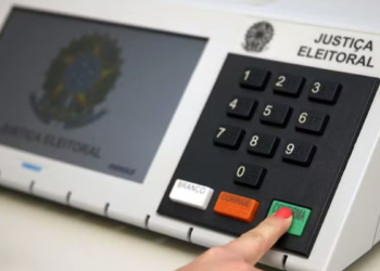 Dedo pressionando a tecla verde Confirma de uma urna eletrônica da Justiça Eleitoral