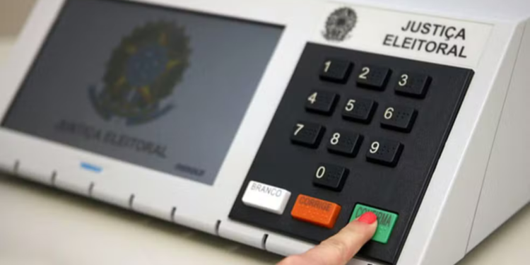 Dedo pressionando a tecla verde Confirma de uma urna eletrônica da Justiça Eleitoral
