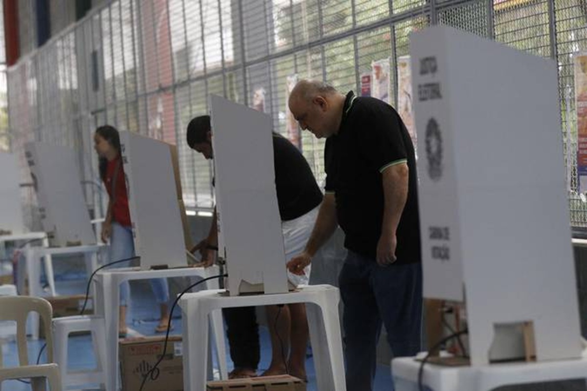 Eleitores de diferentes idades votando em cabines da Justiça Eleitoral montadas em local de votação