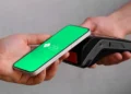 Mão segura celular com tela verde do Pix perto de maquininha de cartão preta.