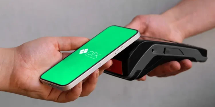 Mão segura celular com tela verde do Pix perto de maquininha de cartão preta.