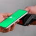 Mão segura celular com tela verde do Pix perto de maquininha de cartão preta.